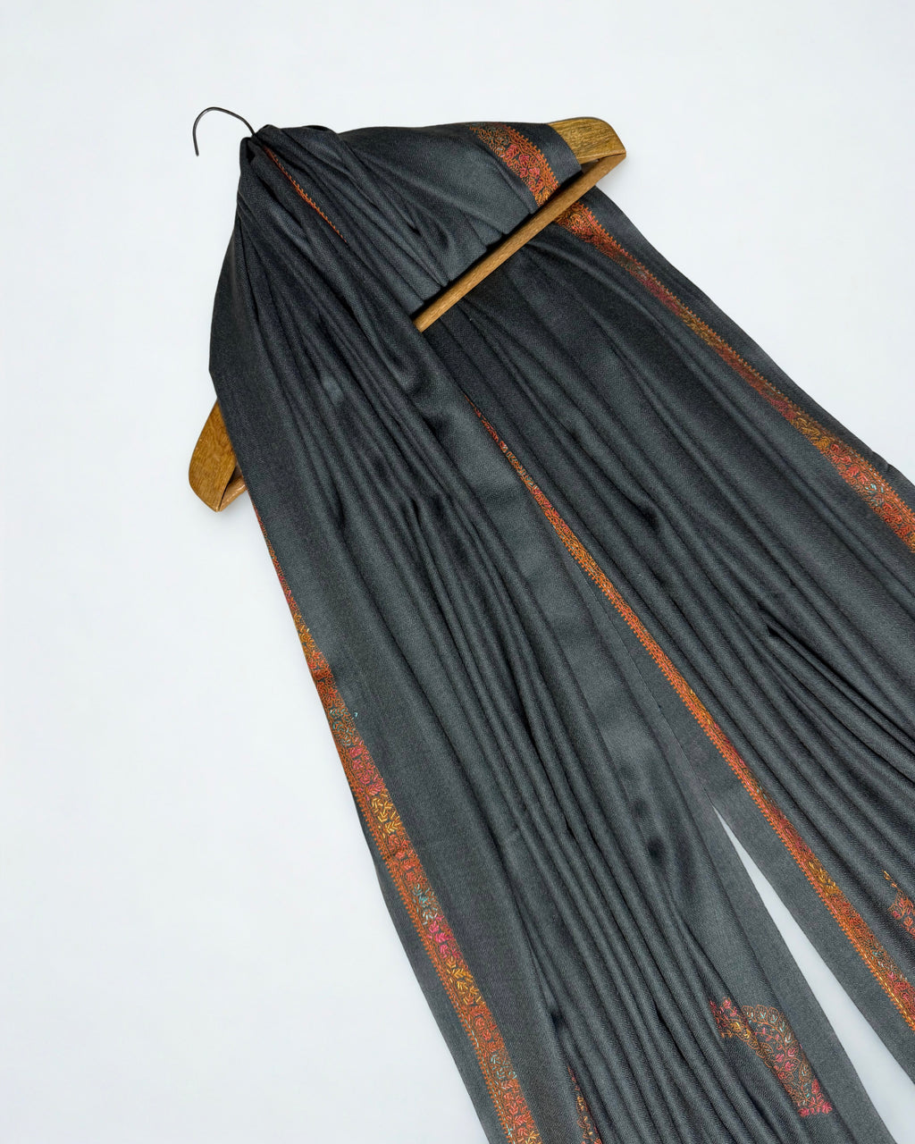 Charcoal Swati Shahtoosh shawl draped over a wooden hanger, rust border through the folds