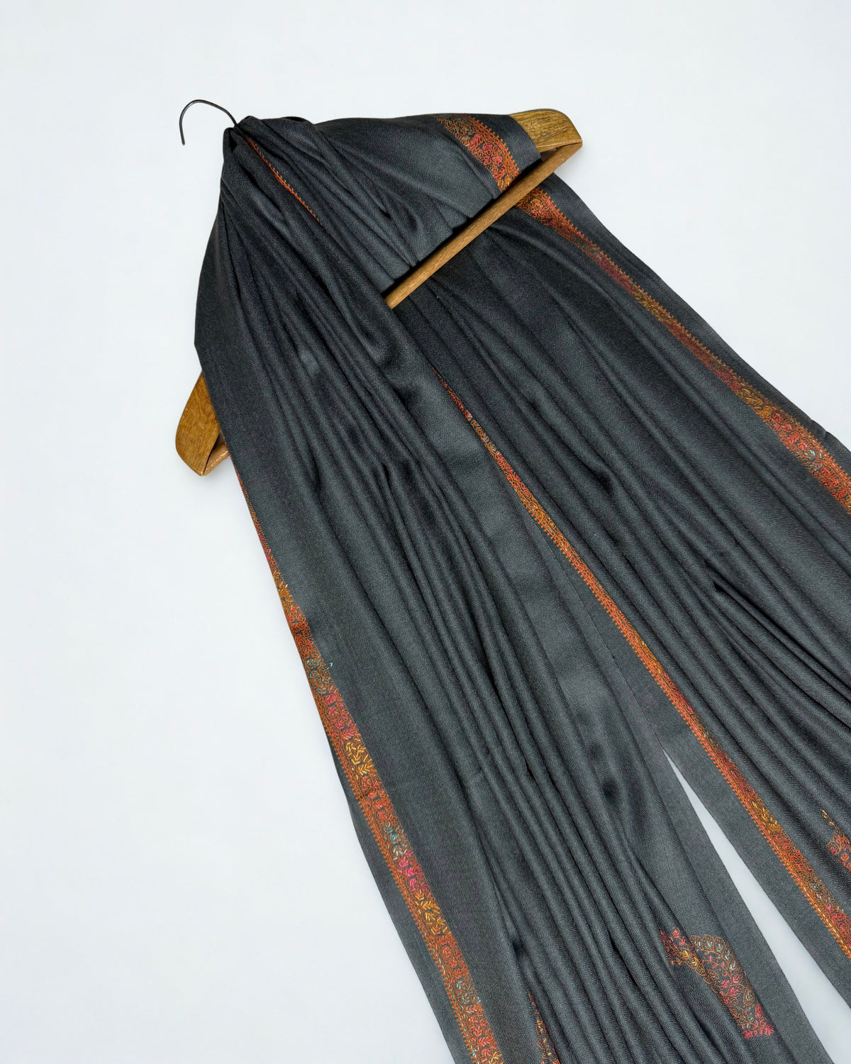 Charcoal Swati Shahtoosh shawl draped over a wooden hanger, rust border through the folds