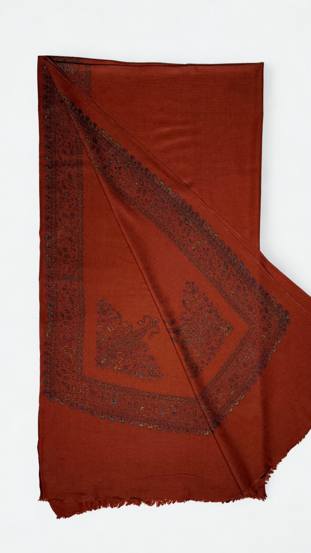 Rust Swati Shahtoosh shawl with one corner turned back, showing the wide hand-embroidered vine border meeting at the corner around a large paisley motif