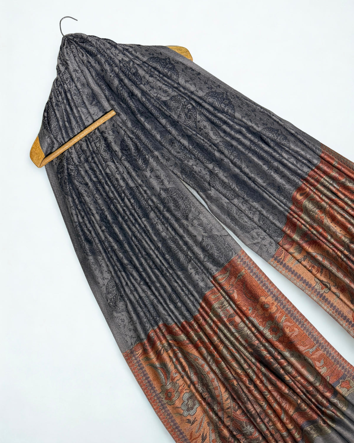 Charcoal Palladar shawl draped on a hanger at an angle, showing the woven paisley field and rust pallas