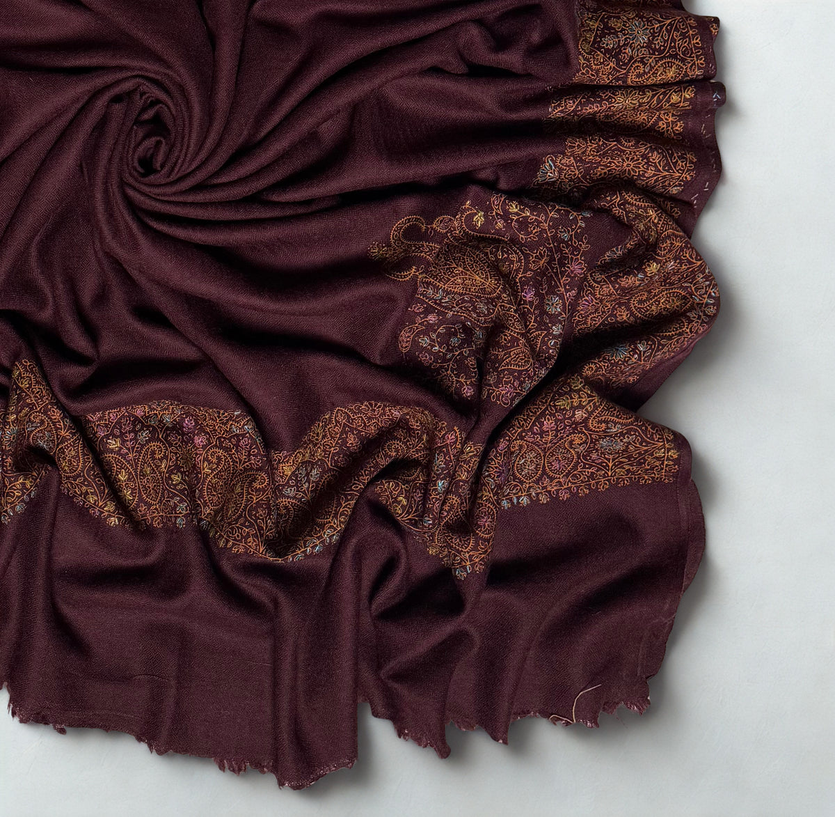 Close view of the deep maroon Swati Shahtoosh shawl gathered in folds, the hand-embroidered paisley band worked in gold, copper, pale blue and rose